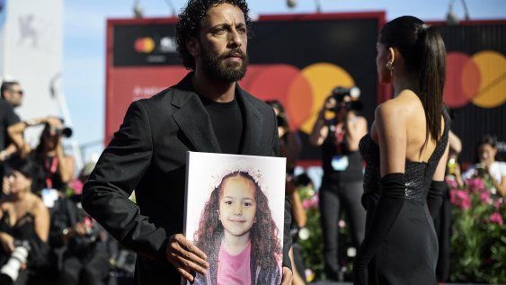 El actor palestino Motaz Malhees muestra una imagen de Hind Rajab a su llegada al estreno de The Voice of Hind Rajab en el 82º Festival de Cine de Venecia.