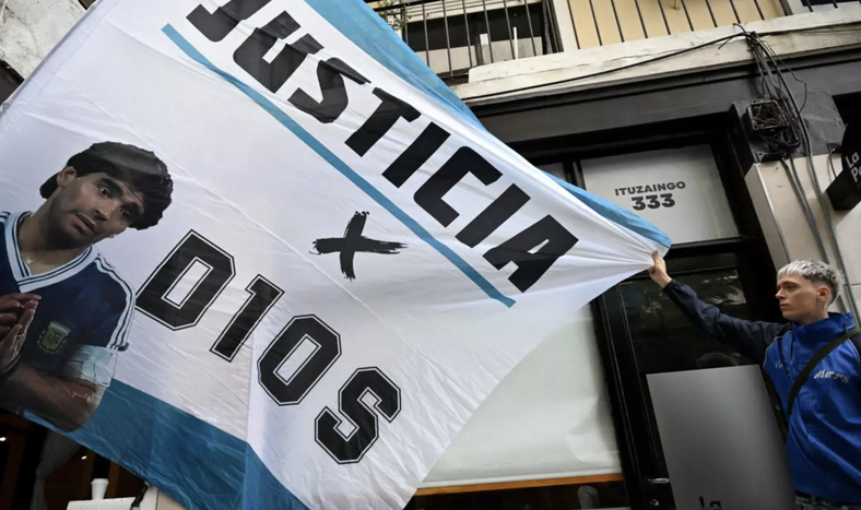 Un aficionado sostiene una bandera con la imagen del fallecido Diego Maradona antes del juicio por la muerte de la leyenda del fútbol argentino Diego Maradona en San Isidro, provincia de Buenos Aires, Argentina, el 11 de marzo de 2025