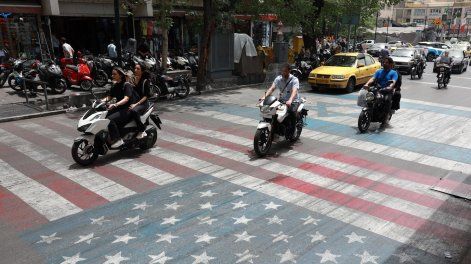 Conductores iraníes pasan por encima de una pintura que representa las banderas de Estados Unidos e Israel en una calle de Teherán, Irán, el 4 de mayo de 2026.