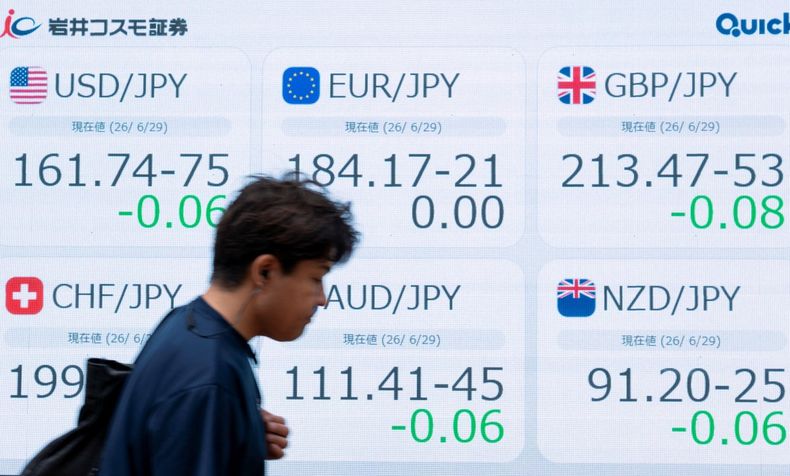 Un hombre pasa junto a un panel electrónico que muestra los tipos de cambio entre el yen y las principales divisas mundiales, incluyendo el tipo de cambio frente al dólar estadounidense (arriba a la izquierda), en una calle de Tokio el 29 de junio de 2026.