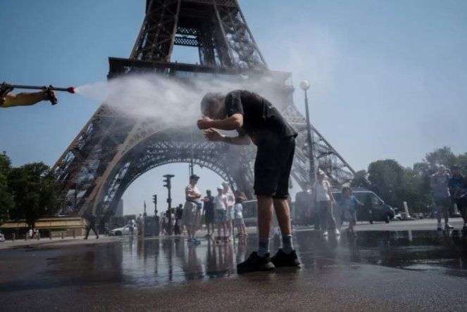 Un empleado municipal rocía agua para refrescar a los turistas frente a la Torre Eiffel en París, el 2 de julio de 2025, mientras una ola de calor azota Francia