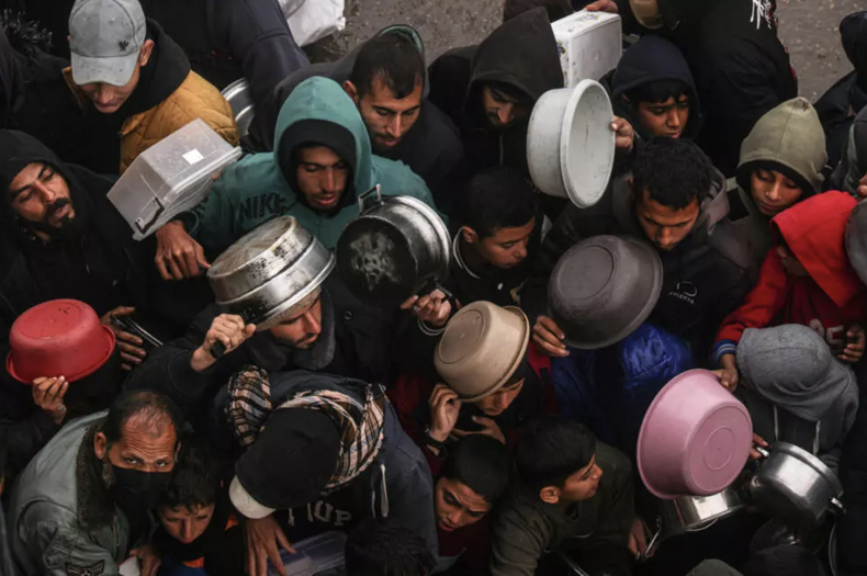 Grupos de palestinos reciben raciones de alimentos en un punto de donación, en un campamento para desplazados internos, en Rafah, en el sur de la Franja de Gaza