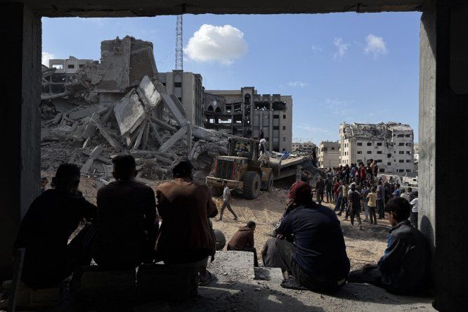 Un grupo de gazatíes observa los trabajos de rescate de cuatro personas (un padre y sus tres hijas), de entre los escombros tras un ataque aéreo israelí contra el edificio donde se refugiaban, 29 de octubre de 2025.