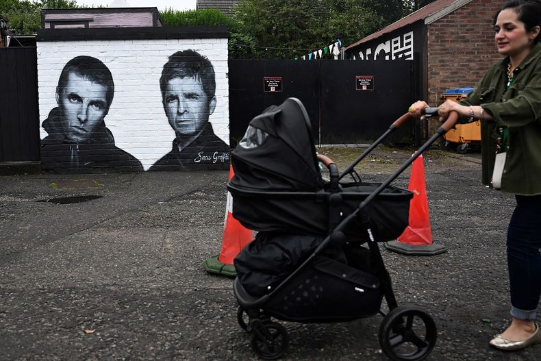 Una mujer empuja un cochecito de bebé junto a un mural de Scott Wilcock, que representa a Liam y Noel Gallagher de Oasis, en el exterior del pub Whitefield, cerca de Heaton Park en Mánchester