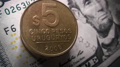 Imagen de un billete de dólares y una moneda de pesos uruguayos.
