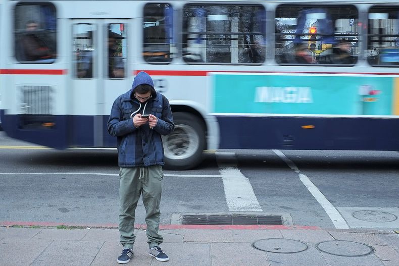 Adolescente mira su celular en el Centro de Montevideo.