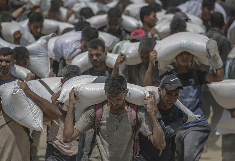 Palestinos desplazados internos cargan sacos de harina cerca de un punto de distribución de alimentos en Zikim, al norte de la Franja de Gaza, el 27 de julio de 2025