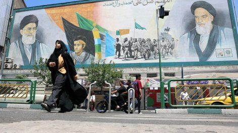 Personas de origen iraní pasan junto a un cartel con imágenes de los difuntos líderes supremos iraníes, el ayatolá Ali Khamenei (arriba a la izquierda) y Ruhollah Khomeini (arriba a la derecha), en una calle de Teherán, Irán, el 18 de mayo de 2026.&nbsp;