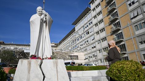 Una mujer reza ante la estatua de Juan Pablo II en el exterior del Hospital Universitario Gemelli, donde el papa León XIV se recupera tras someterse a una intervención quirúrgica para extirpar un tumor canceroso de su pulmón derecho, en Roma, el 14 de octubre de 2026.
