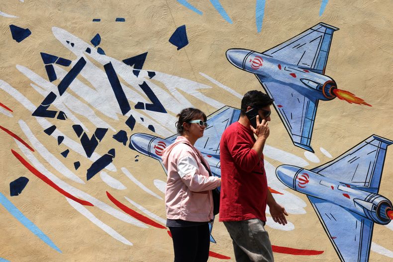 Un hombre y una mujer pasan junto a un mural antiestadounidense y antiisraelí en Teherán, el 21 de abril de 2026, en medio de un alto el fuego en la región.