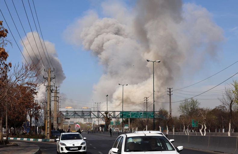 La gente corre en busca de refugio mientras el humo se eleva tras un ataque aéreo en el centro de Teherán, Irán.