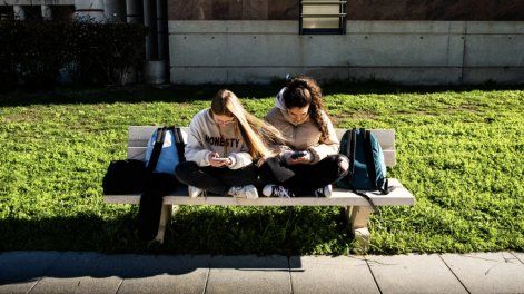 Dos adolescentes miran sus celulares.