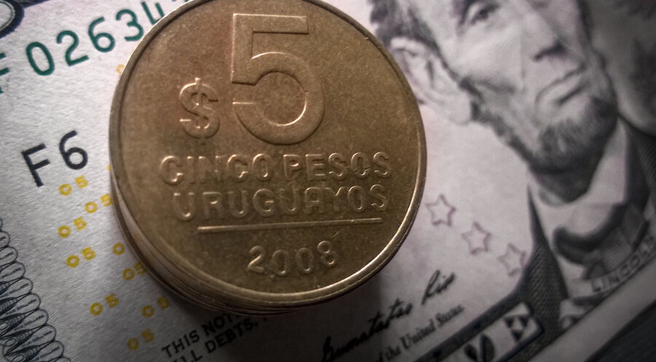 Imagen de un billete de dólares y una moneda de pesos uruguayos.