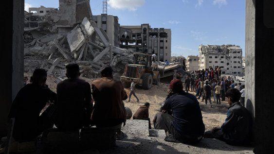 Un grupo de gazatíes observa los trabajos de rescate de cuatro personas (un padre y sus tres hijas), de entre los escombros tras un ataque aéreo israelí contra el edificio donde se refugiaban, 29 de octubre de 2025.