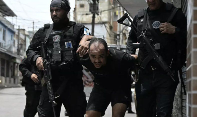 Dos policías brasileños se llevan a un detenido durante la gran operación contra el narcotráfico en Río de Janeiro, el 28 de octubre de 2025 en la favela de Vila Cruzeiro.