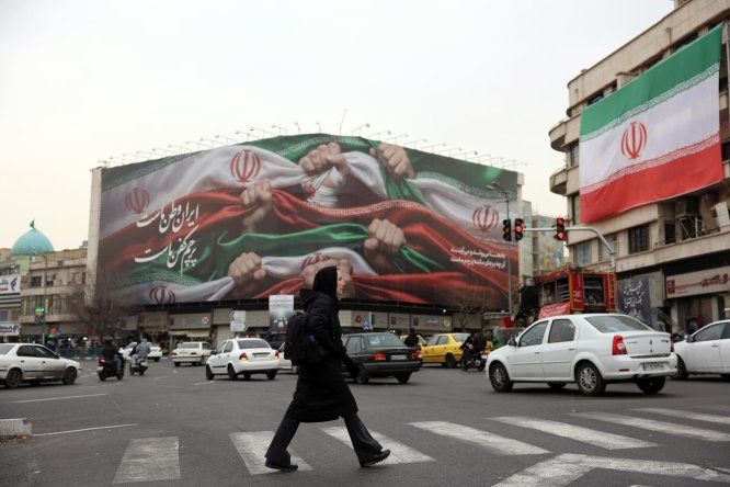 Una mujer iraní cruza una calle cerca de una valla publicitaria que dice “Irán es nuestra Patria” en la Plaza Enqelab de Teherán, Irán, este martes 13 de enero de 2025.