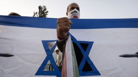 Un hombre iraní, con la bandera de su país, se encuentra detrás de una pancarta antiisraelí durante una manifestación para celebrar el alto el fuego, que considera una victoria sobre Israel en una guerra de 12 días, en el centro de Teherán, Irán, el 24 de junio de 2025