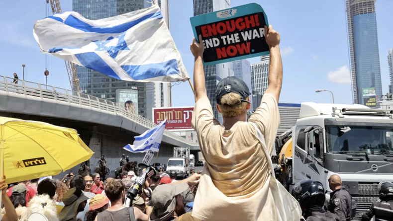 Un manifestante sostiene una pancarta mientras otros bloquean una carretera durante una protesta antigubernamental que exige un acuerdo para liberar a los israelíes detenidos en la Franja de Gaza por militantes de Hamás