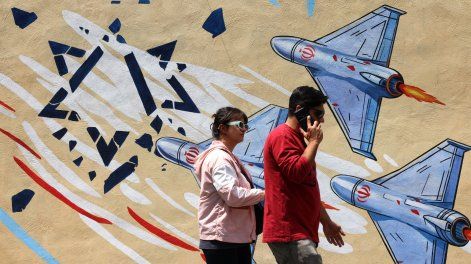 Un hombre y una mujer pasan junto a un mural antiestadounidense y antiisraelí en Teherán, el 21 de abril de 2026, en medio de un alto el fuego en la región.