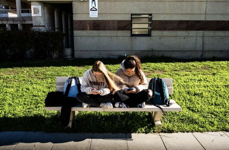 Dos adolescentes miran sus celulares.