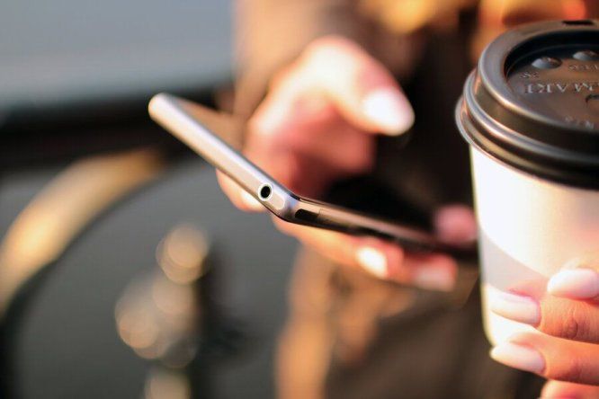Persona sostiene u café mientras revisa su teléfono celular &nbsp;
