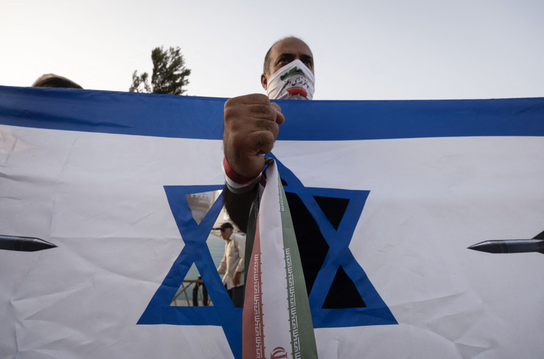 Un hombre iraní, con la bandera de su país, se encuentra detrás de una pancarta antiisraelí durante una manifestación para celebrar el alto el fuego, que considera una victoria sobre Israel en una guerra de 12 días, en el centro de Teherán, Irán, el 24 de junio de 2025