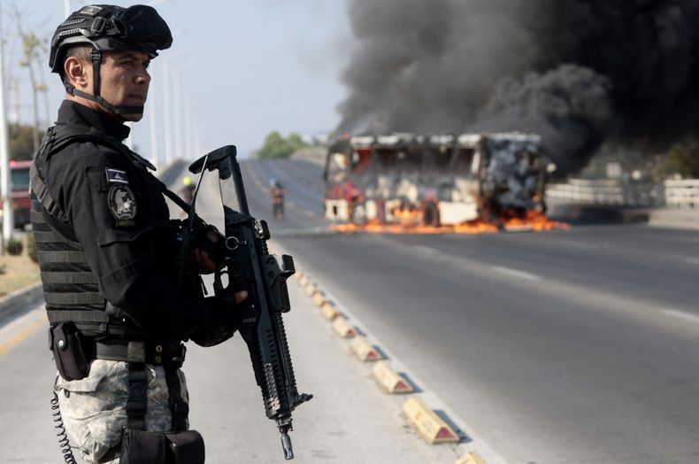 Un agente policial de México vigila un ómnibus incendiado tras una ola de ataques atribuidos al crimen organizado durante un operativo del gobierno realizado en febrero en Jalisco.