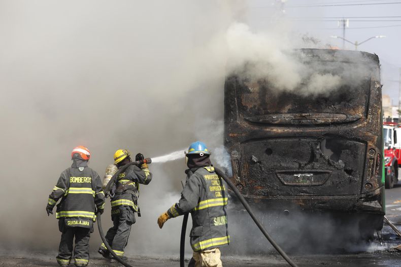 Integrantes del Cuerpo de Bomberos de Guadalajara intentan apagar un vehículo incendiado tras la caída del Mencho.