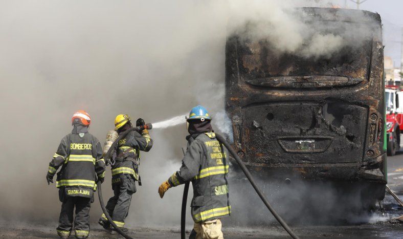 Integrantes del Cuerpo de Bomberos de Guadalajara intentan apagar un vehículo incendiado tras la caída del Mencho.