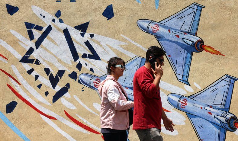 Un hombre y una mujer pasan junto a un mural antiestadounidense y antiisraelí en Teherán, el 21 de abril de 2026, en medio de un alto el fuego en la región.