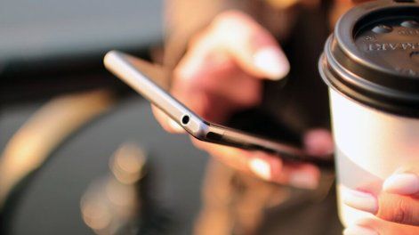 Persona sostiene u café mientras revisa su teléfono celular &nbsp;