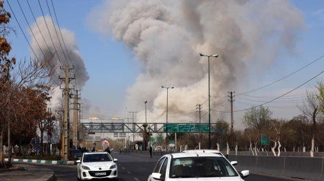 La gente corre en busca de refugio mientras el humo se eleva tras un ataque aéreo en el centro de Teherán, Irán.