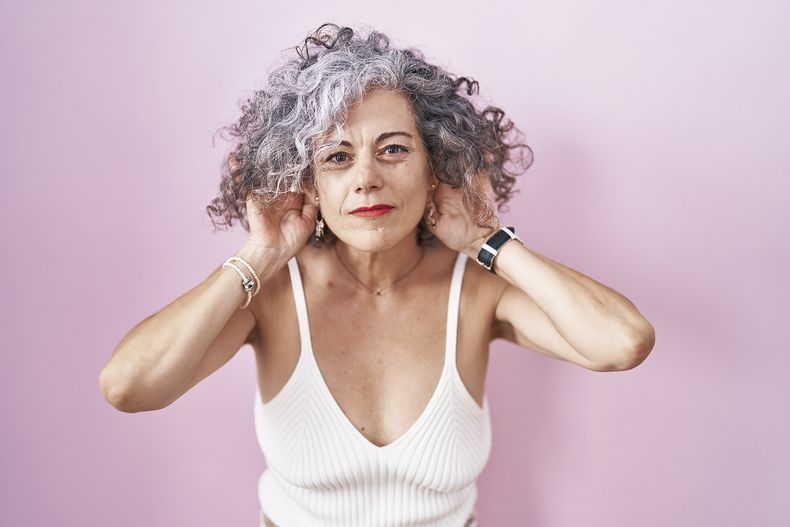 middle-age-woman-with-grey-hair-standing-pink-background-trying-hear-both-hands-ear-gesture-curious-gossip-hearing-problem-deaf.jpg